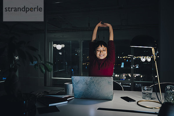 Lächelnde junge Geschäftsfrau dehnt sich bei der späten Arbeit im Coworking Space