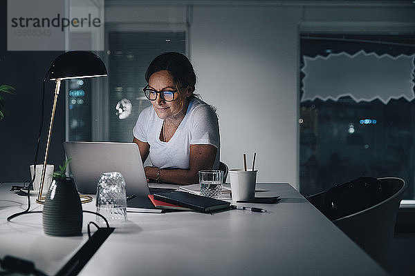 Selbstbewusste Geschäftsfrau mit Laptop bei der Arbeit im Büro in der Nacht