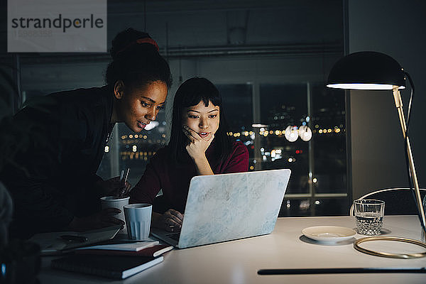 Selbstbewusste Geschäftsfrauen planen ihre Strategie  während sie bei nächtlichen Besprechungen im Büro den Laptop benutzen