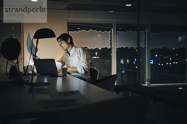 Engagierter männlicher Unternehmer liest Dokument bei der späten Arbeit im dunklen Coworking Space