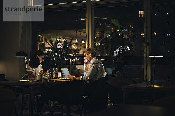 Männliche und weibliche Berufstätige  die spät nachts in dunklen Büros arbeiten