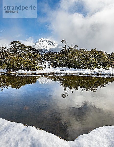 Kleiner Bergsee mit Spiegelung  Ausblick auf wolkenverhangene Berge  Schnee am Gipfel des Key Summit  Mt. Christina  Fiordland Nationalpark  Westküste  Südinsel  Neuseeland  Ozeanien