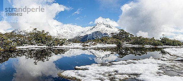 Kleiner Bergsee mit Spiegelung  Ausblick auf wolkenverhangene Berge  Schnee am Gipfel des Key Summit  Mt. Christina  Fiordland Nationalpark  Westküste  Südinsel  Neuseeland  Ozeanien