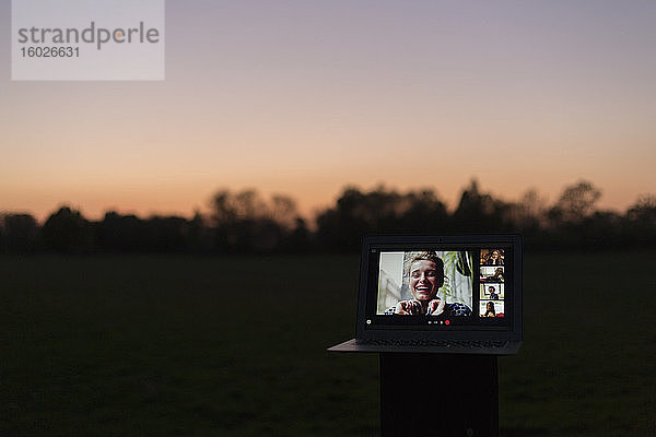 Video-Chat mit Freunden auf Laptop-Bildschirm im Park bei Dämmerung