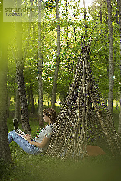 Frau mit Laptop am Ast-Tipi im Wald