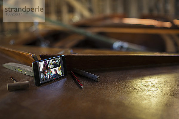 Video-Chat unter Kollegen auf dem Bildschirm eines Smartphones auf einem Holzboot