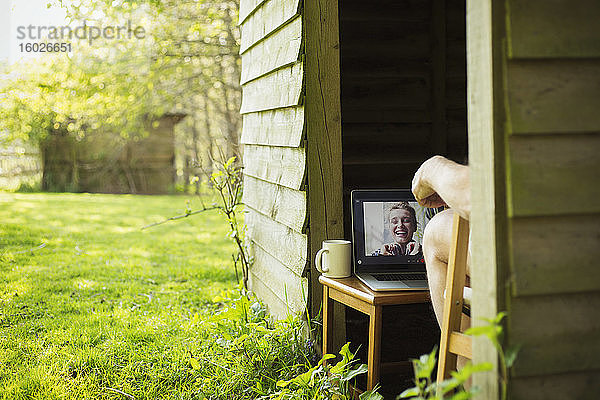 Mann Video-Chat mit Freunden auf Laptop vom Gartenschuppen