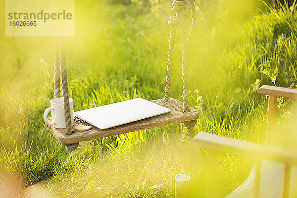 Laptop und Kaffeetasse auf der Schaukel im sonnigen Garten