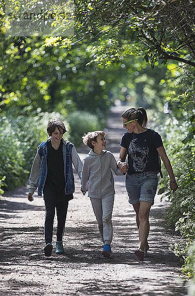 Mutter und Söhne gehen auf dem sonnigen Parkweg