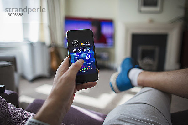 POV Mann regelt die Temperaturregelung am Smartphone im Wohnzimmer