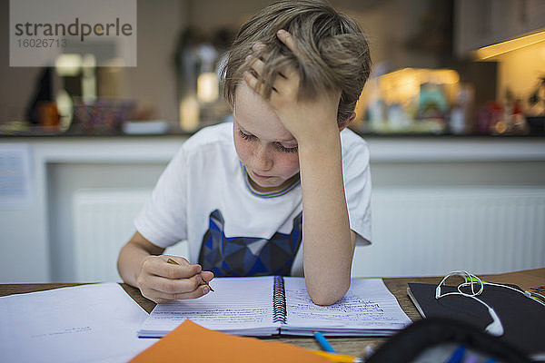 Fokussierter Junge macht Hausaufgaben bei Tisch