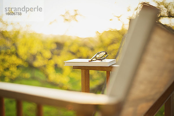 Buch und Brille auf Rasenstuhl im sonnigen Garten