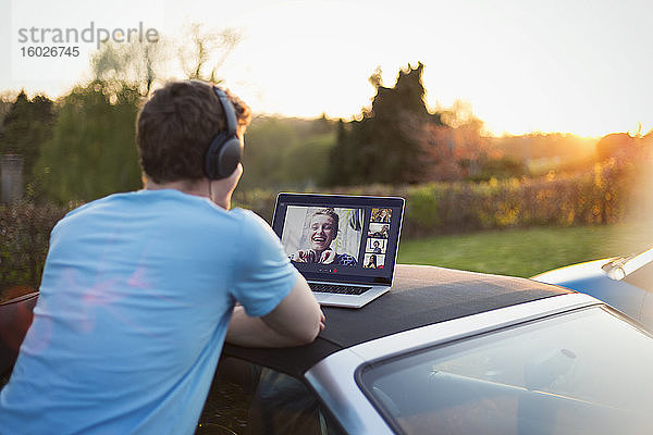 Mann mit Kopfhörern und Laptop beim Video-Chat mit Freunden auf dem Autodach