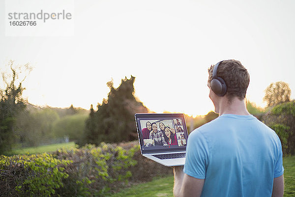 Mann mit Kopfhörern beim Video-Chat mit Freunden im sonnigen Garten