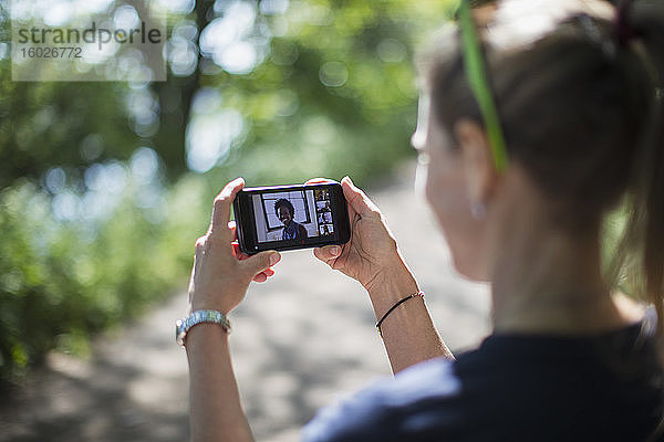 Frau im sonnigen Park im Video-Chat mit Freunden auf dem Bildschirm eines Smartphones