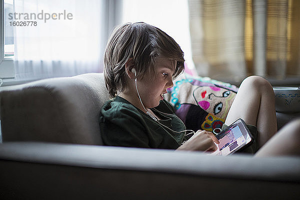 Junge mit Kopfhörern mit digitalem Tablet im Wohnzimmer