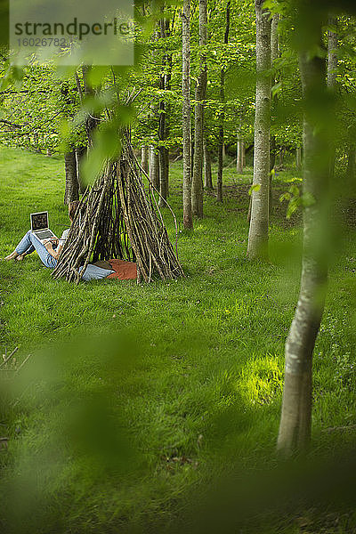 Frau mit Laptop am Ast-Tipi im Wald