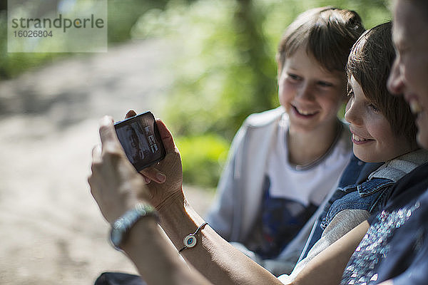 Mutter und Söhne videochatten mit Freunden per Smartphone im Park