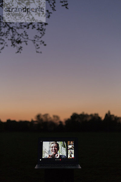 Video-Chat mit Freunden am Laptop-Bildschirm im Garten in der Abenddämmerung