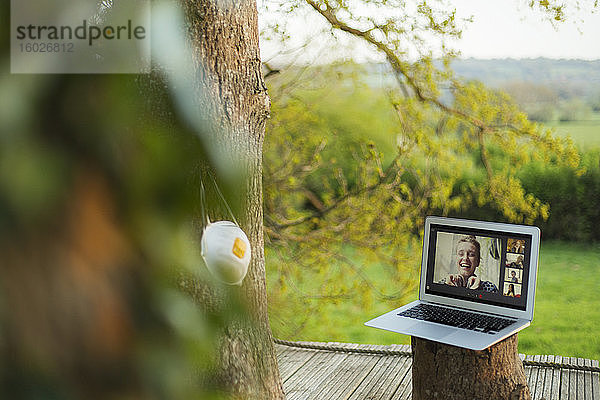 Gesichtsmaske  die am Baum neben Freunden hängt Video-Chat am Laptop