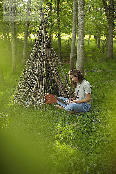 Frau mit Laptop entspannt sich am Ast-Tipi im Wald