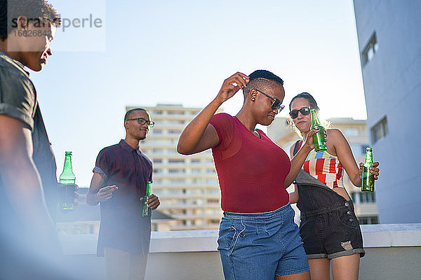 Unbeschwerte junge Freunde tanzen und trinken Bier auf dem Dach der Stadt
