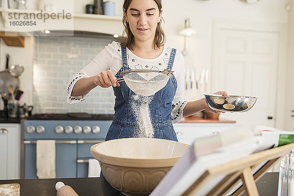 Teenager-Mädchen sichtet Mehl zum Backen in der Küche