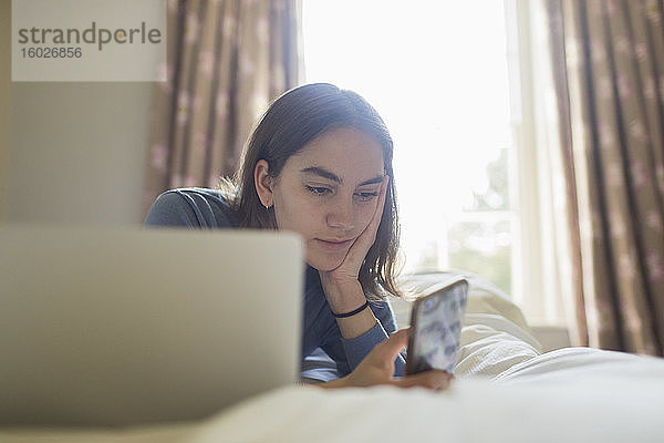 Teenagerin benutzt Smartphone am Laptop im Bett