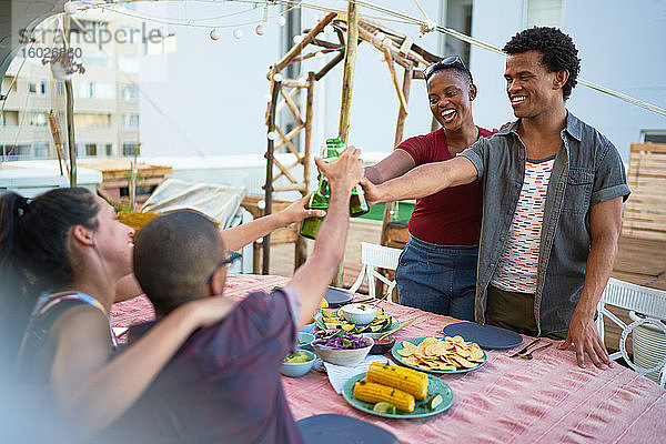 Glückliche junge Freunde trinken Bier und essen auf der Terrasse zu Mittag