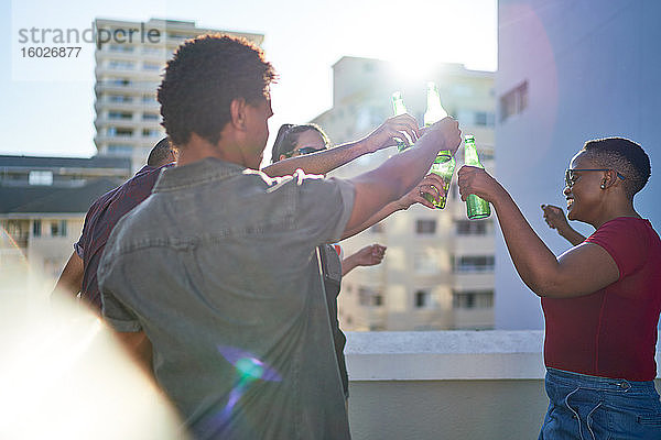 Glückliche junge Freunde tanzen und trinken Bier auf dem sonnigen Dach