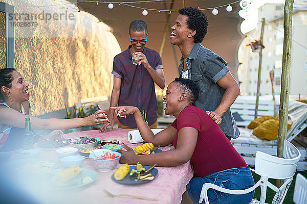 Glückliche junge Freunde mit Smartphone beim Mittagessen am Terrassentisch