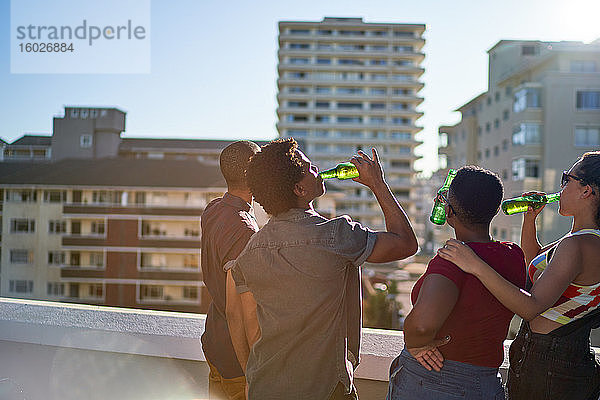 Junge Freunde trinken Bier auf dem sonnigen Stadtdach