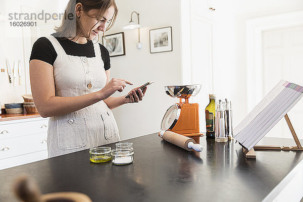 Teenagerin mit Smartphone backt in der Küche