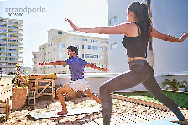 Junges Paar praktiziert Yoga auf sonnigem Stadtbalkon auf dem Dach