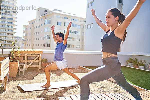 Junges Paar praktiziert Yoga auf sonnigem städtischen Dachbalkon