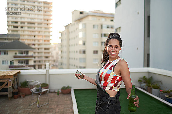 Porträt einer selbstbewussten jungen Frau mit Smartphone und Bier auf dem Dach