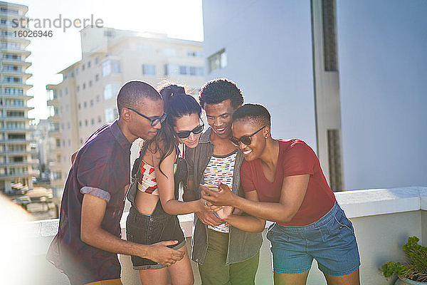 Junge Freunde nutzen Smartphone auf sonnigem Dachbalkon