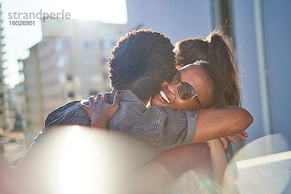 Glückliches junges Paar umarmt sich auf sonnigem Stadtbalkon