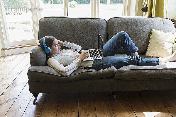 Teenagerin mit Kopfhörern und Laptop Video-Chat auf Wohnzimmersofa