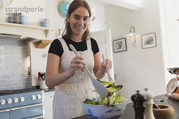 Porträt einer selbstbewussten Teenagerin  die in der Küche Salat macht