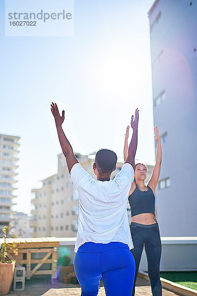 Junge Frauen praktizieren Yoga auf dem sonnigen städtischen Dachbalkon