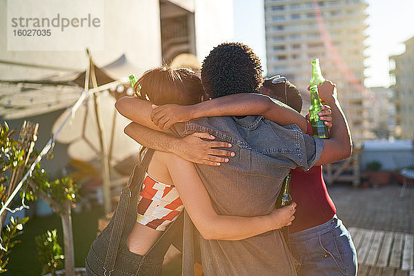 Glückliche junge Freunde umarmen sich und trinken Bier auf dem sonnigen Dach