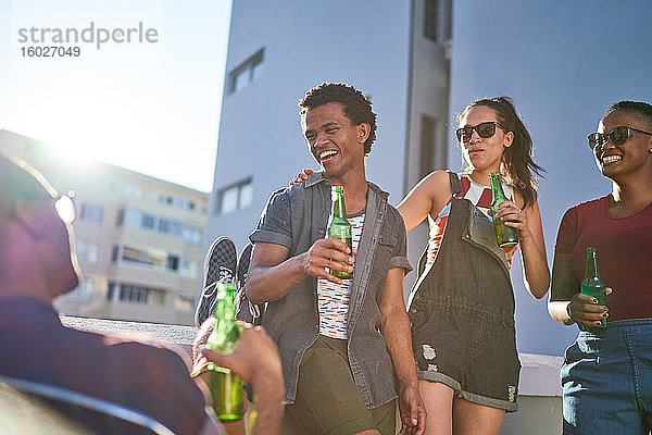 Glückliche junge Freunde trinken Bier auf dem sonnigen Stadtbalkon