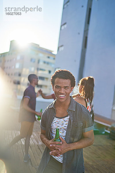 Porträt eines glücklichen jungen Mannes beim Biertrinken auf dem sonnigen Stadtdach