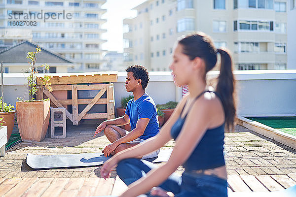 Junger Mann und Frau praktizieren Yoga auf einem sonnigen städtischen Dach