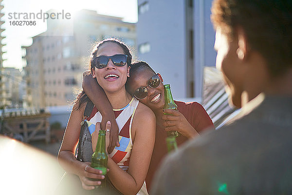 Glückliche junge Freundinnen trinken Bier auf einem sonnigen Sommerdach