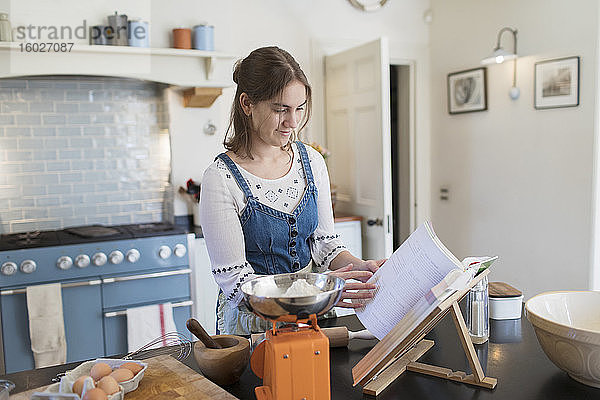 Teenagerin mit Kochbuch beim Backen in der Küche