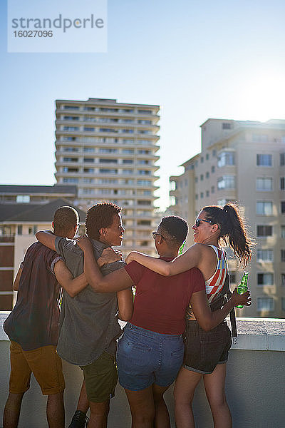 Glückliche junge Freunde hängen auf dem sonnigen Balkon auf dem städtischen Dach herum