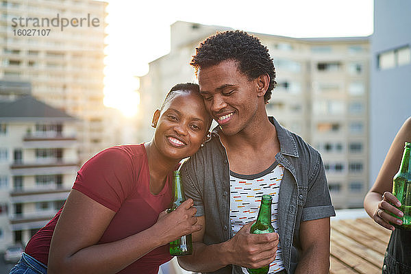 Porträt eines glücklichen jungen Paares beim Biertrinken auf dem sonnigen Dachbalkon