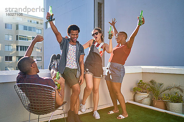 Fröhliche junge Freunde jubeln und trinken Bier auf dem Dach der Stadt